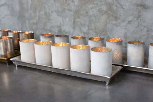 The Wilder Mercury Glass Candle Holder sits on an aluminum tray in two lengths and is available in a gold or silver finish. The Wilder Candle Holder Tray and Mercury Votive Set comes as a set of 5 Mercury Glass Candle Holders and sits on a 20" tray and the 34" tray holds 9 Mercury Votive Holders. Use the Wilder Mercury Glass Candle Holders spread throughout a room for subtle sparkle in your space. Line the Mercury Votives on the tray and use in uniform multiples on a dining table. The Wilder Aluminum Tray and Mercury Votives look amazing lining a mantle or cocktail table and each tray has an inset for each votive. Available in sets of multiples, the candle light options are endless for these classic Aluminum Candle Trays and Mercury Glass Votives.
